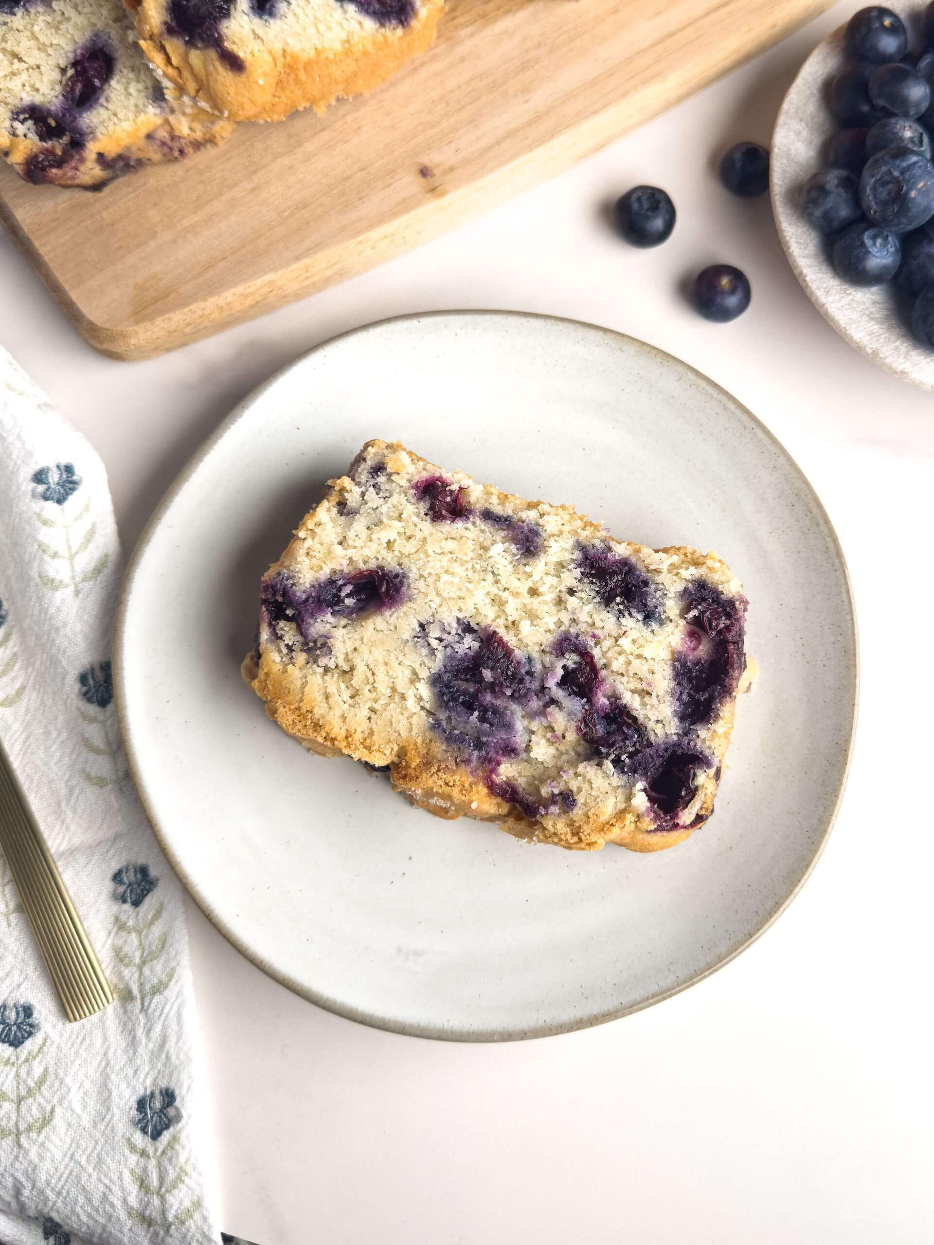 Slice of homemade blueberry bread with a golden crust and moist, fluffy interior, packed with fresh blueberries—perfect for breakfast or a sweet treat.
