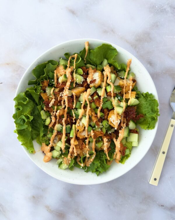 Bowl of crispy rice and spicy chicken on lettuce with sesame seeds, cucumber, and spicy mayo